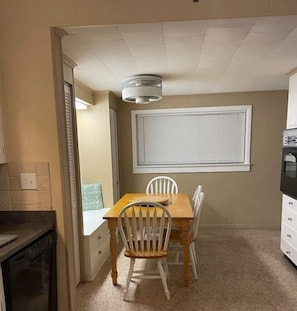 Enjoy meals in this cozy dining area with a table and chairs, a window with blinds, and a partial view of the kitchen.