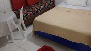 Une petite pièce propre, avec un lit, une chaise, une table et un tapis rouge.