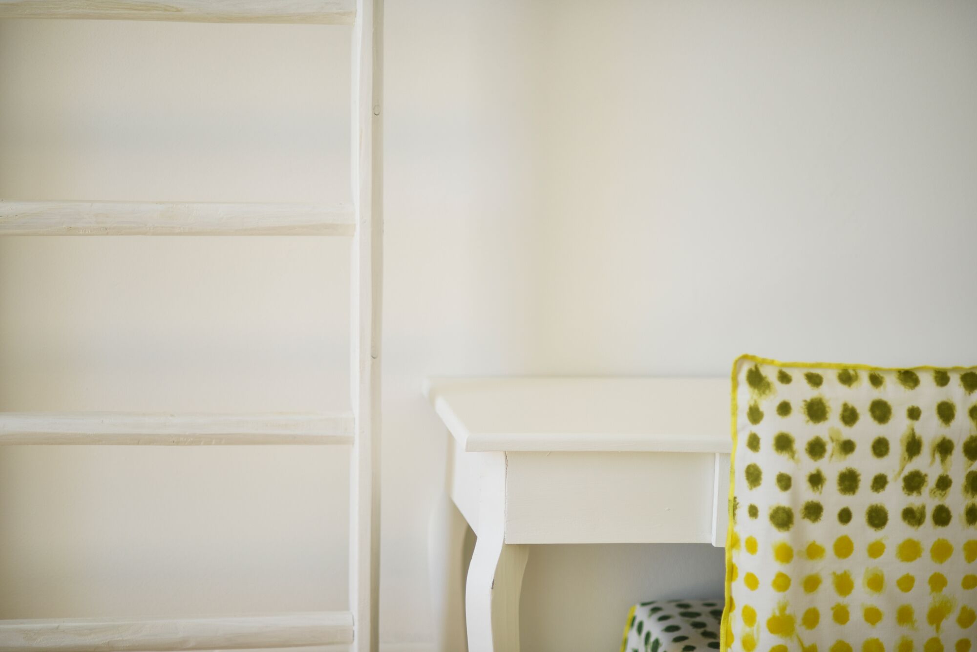 Een witte muur met een witte deur en een witte tafel met een patroonrijk kleed.