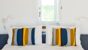 A bedroom with a bed, two pillows with abstract patterns, a window, and a wall-mounted light fixture. - Masseria Torrechiara Eco Dimora di Charme. (Corato)
