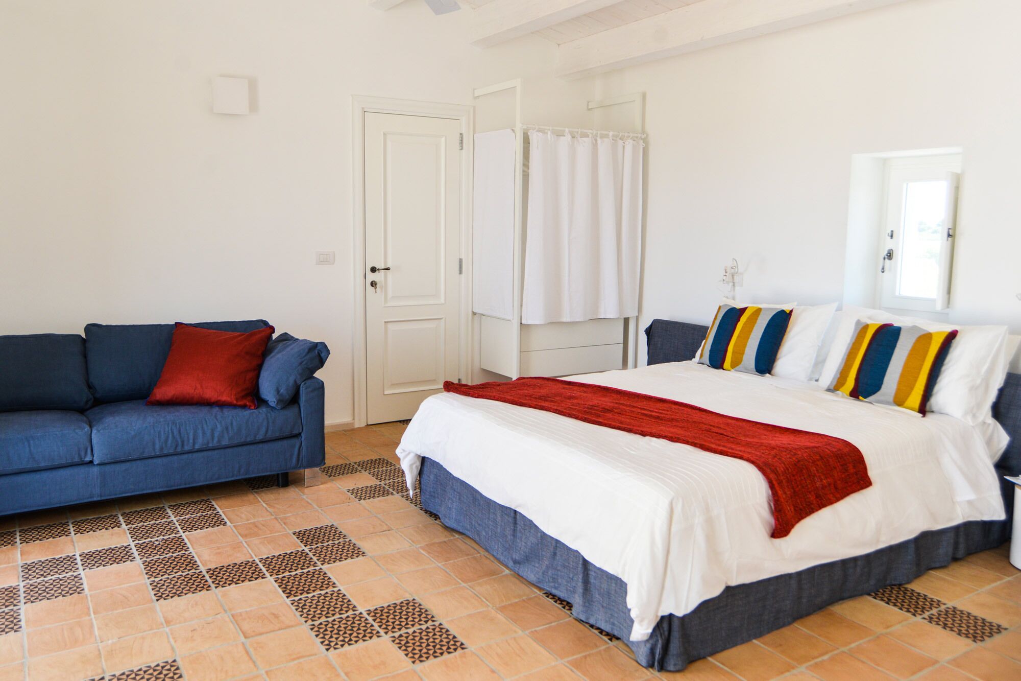 A bedroom with a bed, a blue sofa, and a white door.