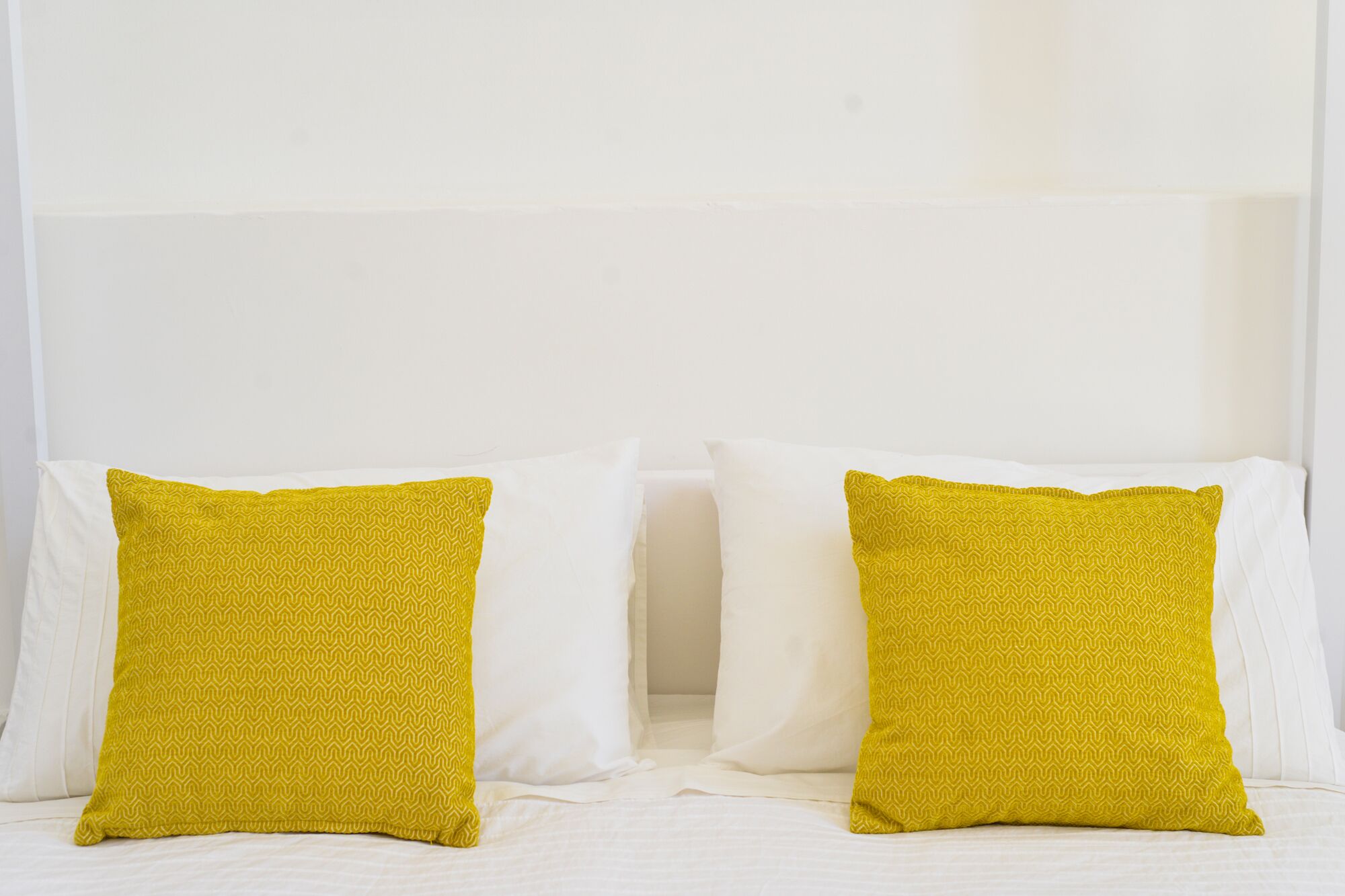 Een bed met twee kussens, één geel en één wit, tegen een effen muur.