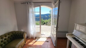 Ein Zimmer mit einem grünen Sofa, einem Klavier und einer Tür, die zu einer schönen Aussicht ins Freie führt.