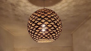 Ein Zimmer mit einer einzigartigen, kugelförmigen Pendelleuchte, einem Holztisch mit einer Vase und einem Blick auf eine Gitarre im Hintergrund.