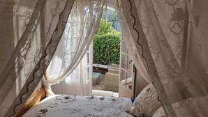 Ein Schlafzimmer mit einem Bett, weißen Vorhängen und Blick auf einen Garten.