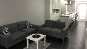 Un salon moderne avec un canapé gris, une table basse blanche et un coin cuisine à l’arrière-plan.