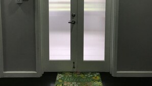 Une porte à deux battants avec des panneaux en verre dépoli, un paillasson orné de motifs floraux et un luminaire fixé au mur.