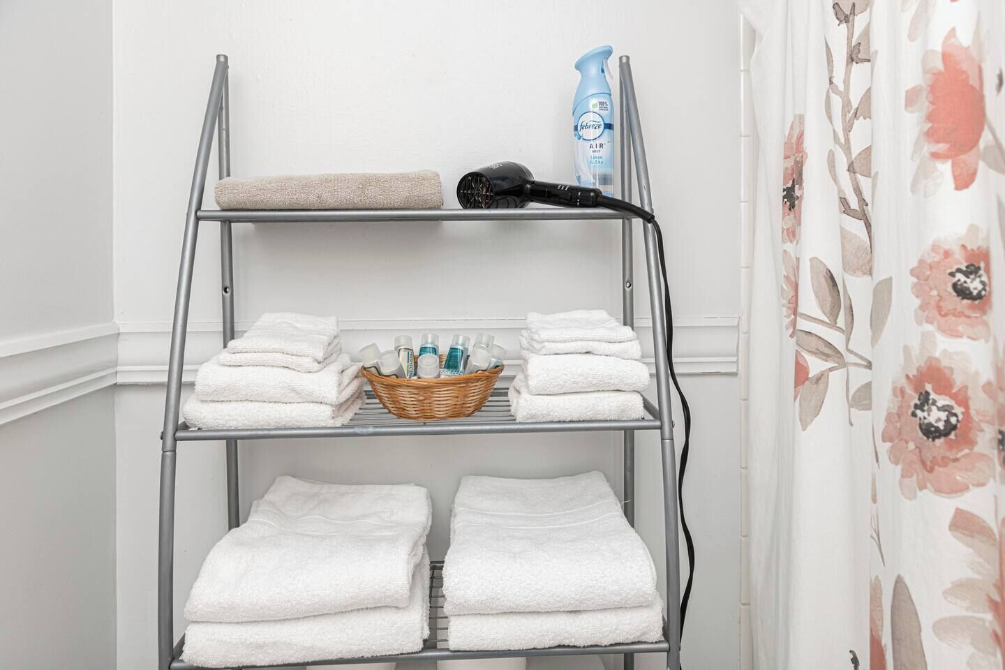 Un étendoir métallique avec des serviettes blanches et un panier contenant des articles de toilette.