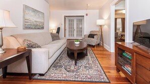A living room with a sofa, armchair, coffee table, and a TV stand. - Bryn Mawr Has It All (Bryn Mawr)