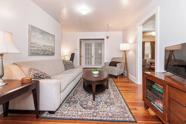 A living room with a sofa, armchair, coffee table, and a TV stand. - Bryn Mawr Has It All (Bryn Mawr)