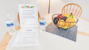 A hotel room with a welcome sign, a fruit basket, and two bottles of water on the table.