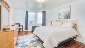 A bedroom with a bed, dresser, chair, and a radiator.