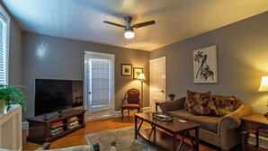 Un salon comprenant un téléviseur, un ventilateur de plafond, un canapé, une table basse et un fauteuil.