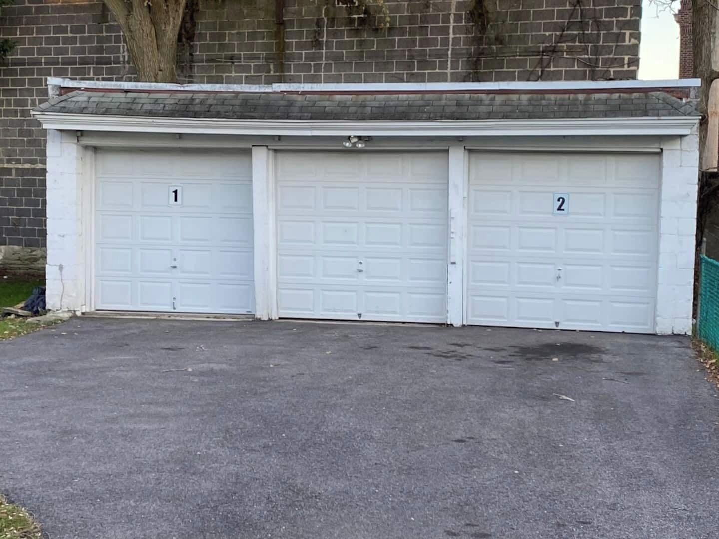 Un garage con tre porte numerate, un muro in mattoni e un albero.