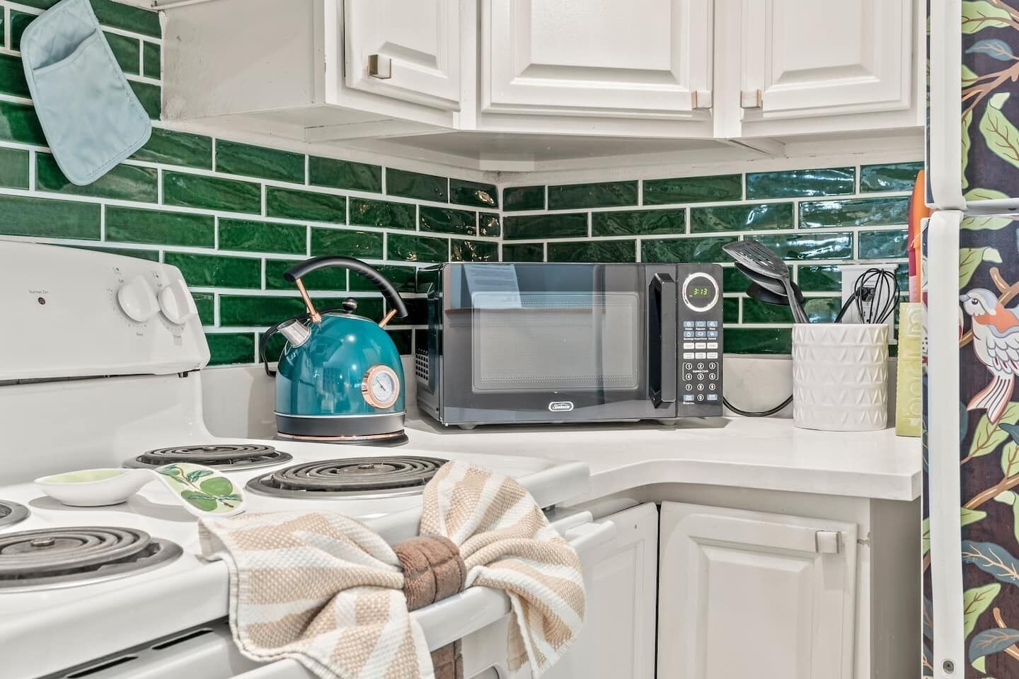Una cucina con fornello, bollitore, microonde e un altro bollitore sul piano di lavoro.