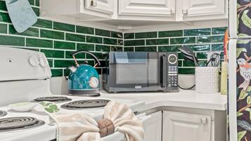 Una cucina con fornello, bollitore, microonde e un altro bollitore sul piano di lavoro.