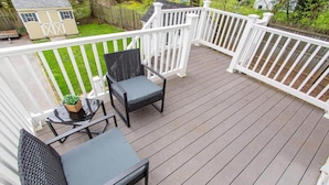A wooden deck with two black wicker chairs and a small table, surrounded by white railings. - Stay At Our Tasteful, Private, & Elegant Abode (Devon)