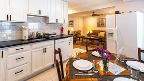 A modern kitchen with white cabinets, a black countertop, and a dining area with a wooden table set for four. - Devon - Horse Show, History, Walk to Shops, Café's (Devon)