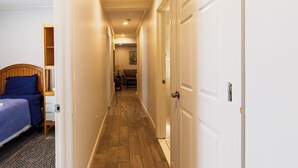 A narrow hallway with a wooden floor, a bed with blue bedding, a nightstand, and a door leading to another room. - Devon - Horse Show, History, Walk to Shops, Café's (Devon)