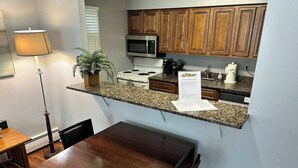 A compact kitchen with wooden cabinets, a microwave, stove, and a granite countertop. - Comfy 2 BR Mid Term Apartment (Narberth)