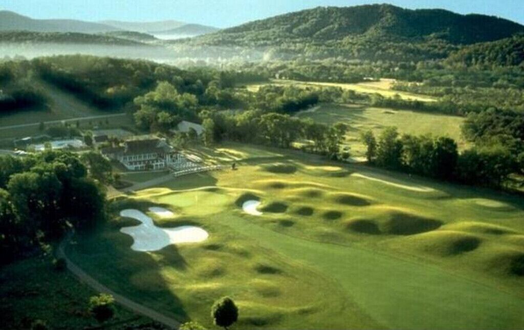 A golf course with bunkers, a clubhouse, and a lake in the background.