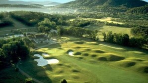 En golfbane med bunkere, et klubhus og en sø i baggrunden.