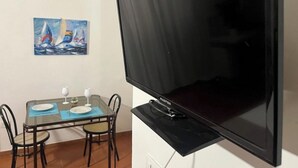 Une pièce dotée d’un grand téléviseur à écran plat fixé au mur, d’une table à manger avec des chaises et de deux tableaux accrochés au mur.