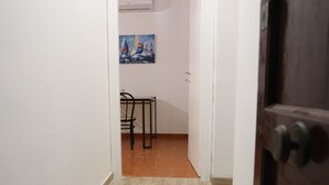Un couloir étroit, dont le sol est recouvert de carreaux, mène à une pièce où un tableau est accroché au mur.