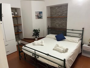 A neatly made bed with white linens and a blue pillow, a potted plant, and a stone wall in the background. - Gate 2 (Tropea)