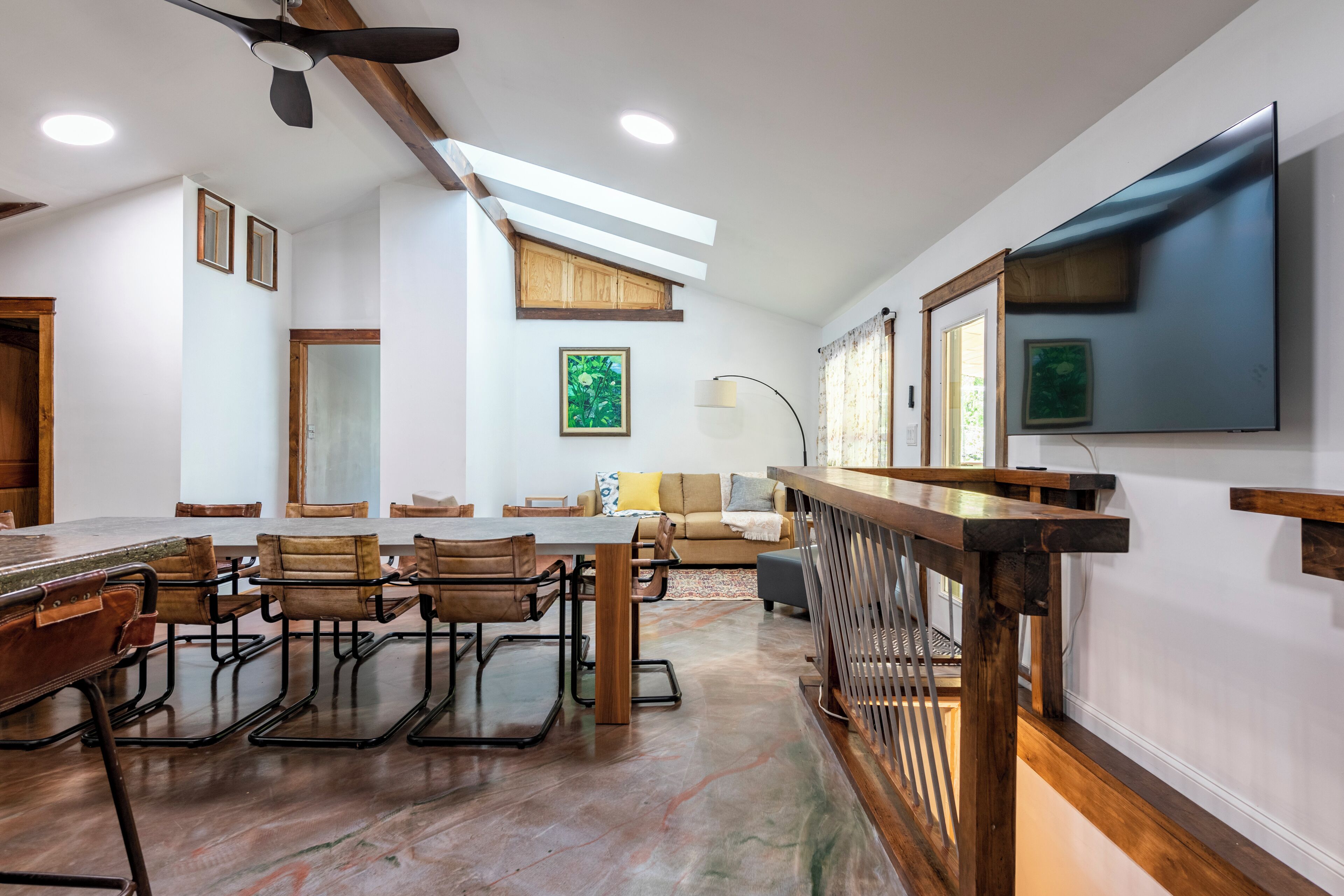A spacious room with a dining area, a sofa, and a TV mounted on the wall.