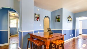 Un coin repas avec une table en bois et des tabourets de bar, des lambris bleus et des œuvres d’art encadrées accrochées aux murs.