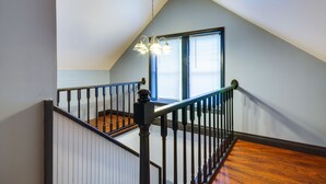 Un escalier doté d’une rampe en bois et de balustres noires, menant à un palier d’où l’on peut admirer une fenêtre avec des stores.