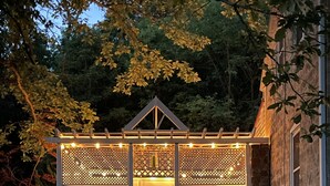 A small, wooden structure with a porch and a lattice door, surrounded by a stone wall and a white picket fence. - Whole House Rental - Private Cottage near Historic Hermann, Missouri (Hermann)