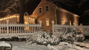 A two-story stone house with a white picket fence, snow-covered bushes, and string lights. - Whole House Rental - Private Cottage near Historic Hermann, Missouri (Hermann)