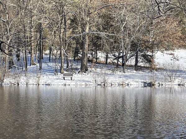 A serene winter scene with a snow-covered landscape, a calm lake, and a bench by the water.