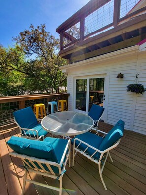 A covered outdoor deck with a glass-top table and four chairs, a hanging flower pot, and a sliding glass door leading to an interior space. - Colby Cottage in Taylors Falls, 4 Bedroom Home - Walk to Interstate Park (Taylors Falls)