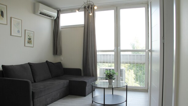 A modern living room with a sectional sofa, a glass coffee table, and a balcony with a view. - Central New Flat. AC, Park View , 2 Rooms (Warszawa)