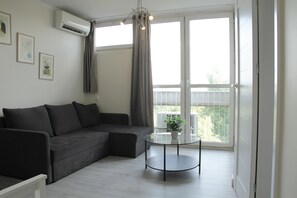 A modern living room with a sectional sofa, a glass coffee table, and a balcony with a view. - Central New Flat. AC, Park View , 2 Rooms (Warszawa)