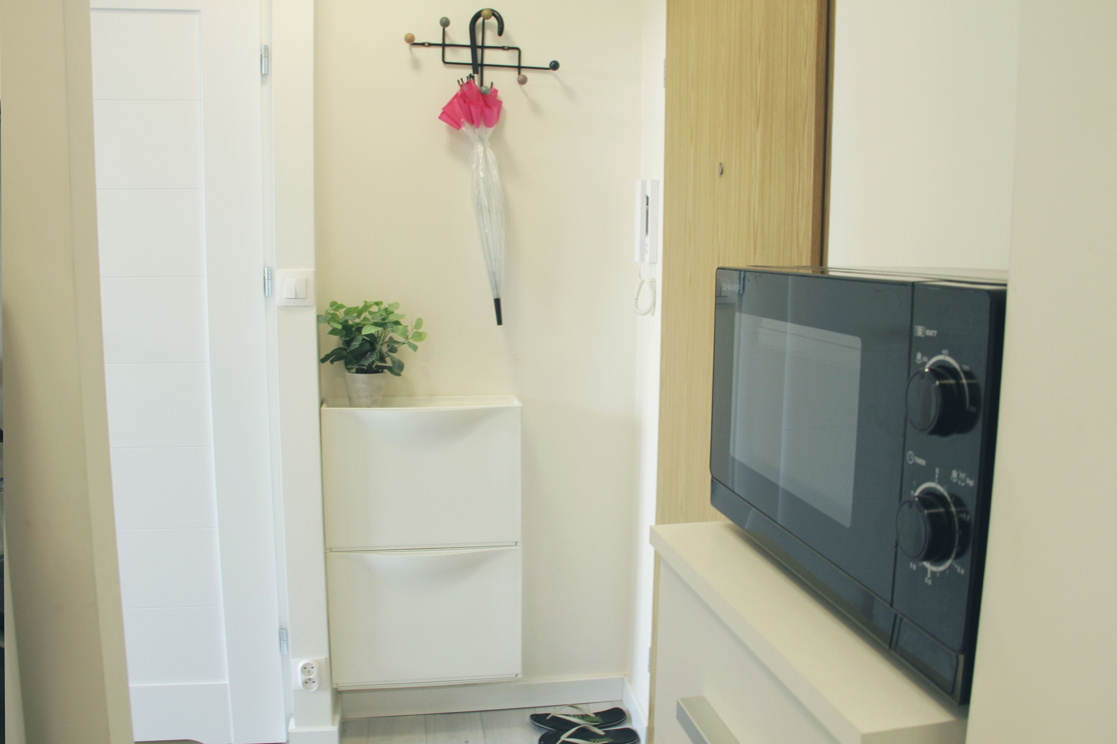 A small kitchenette with a microwave, a white cabinet, and a plant on a shelf.