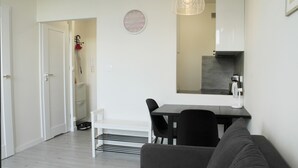 A modern living room with a sofa, a dining table with chairs, a coffee machine, and a kitchen area in the background. - Central New Flat. AC, Park View , 2 Rooms (Warszawa)