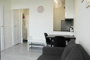A modern living room with a sofa, a dining table with chairs, a coffee machine, and a kitchen area in the background.