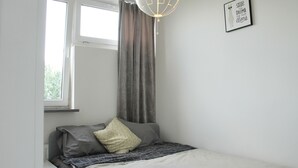 A bedroom with a bed, a window with curtains, a wall-mounted light fixture, and a framed quote on the wall. - Central New Flat. AC, Park View , 2 Rooms (Warszawa)