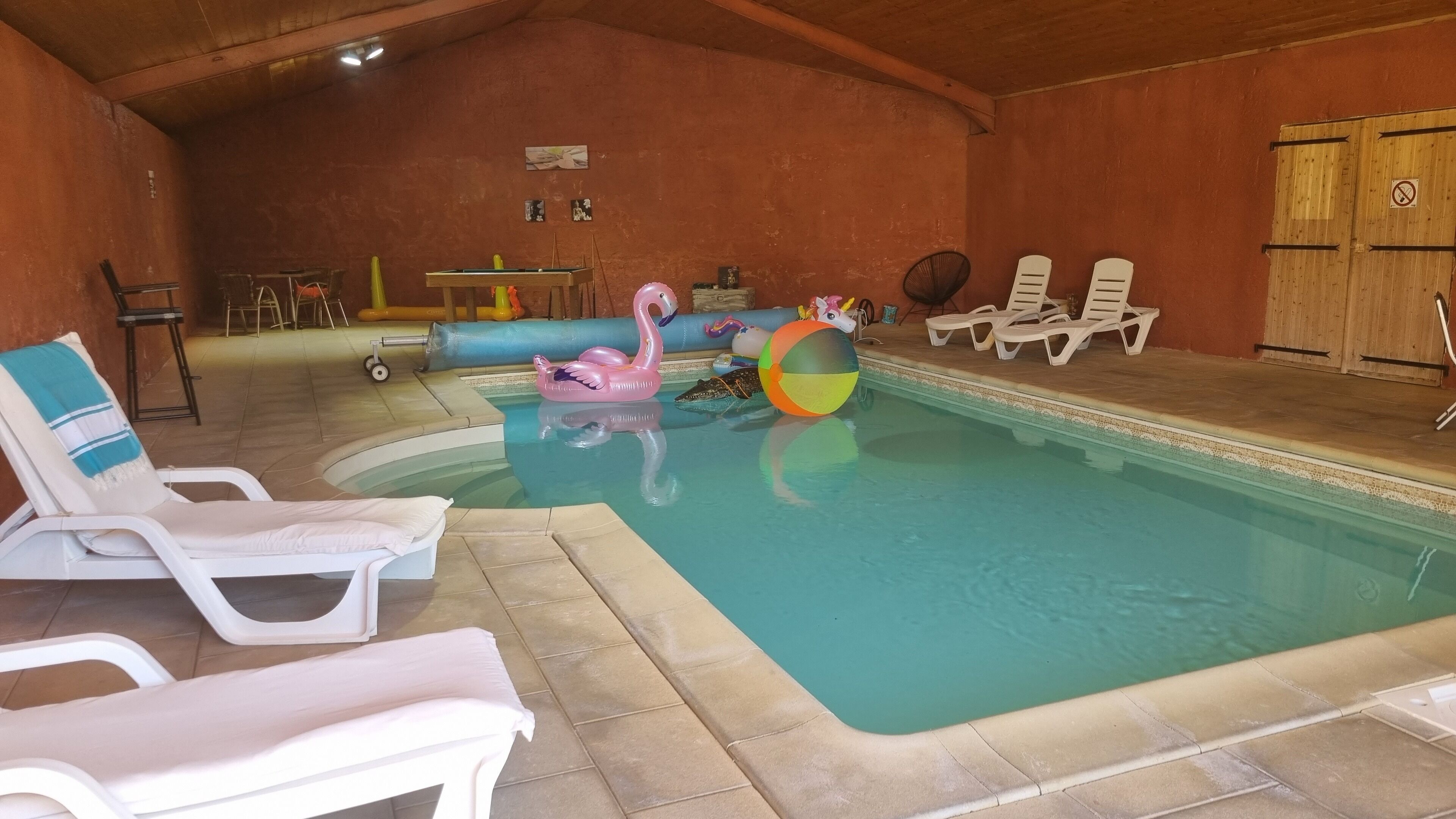 Une piscine intérieure avec des chaises longues, une table de billard et des jeux gonflables.