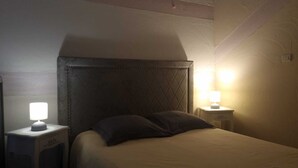 Una cama individual con cabecera acolchada, dos lámparas de noche y una mesita.