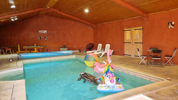 Una piscina interior con techo de madera, mesa de billar y sillones de descanso.
