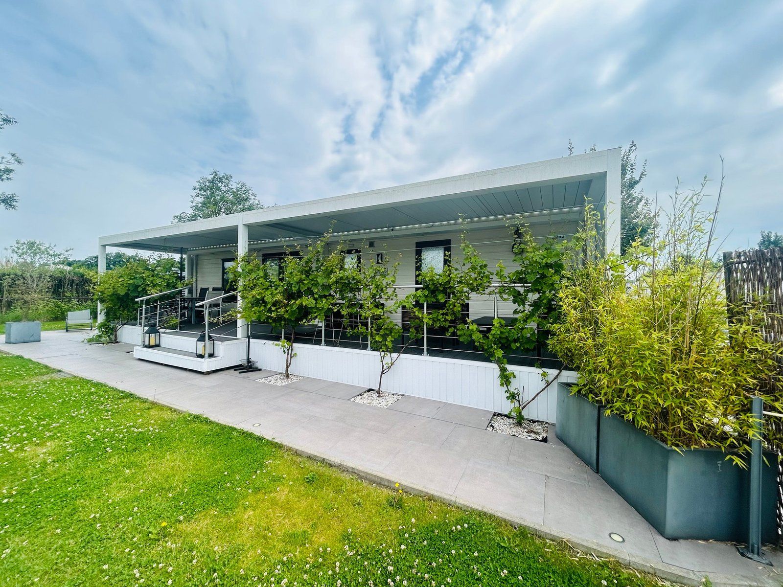 A modern building with a covered outdoor area, a staircase, and a well-maintained lawn.