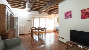 A spacious living area with a wooden ceiling, a dining table with chairs, a sofa, a flat-screen TV, and a kitchen area with a refrigerator and cabinets. - Residence Antico Borgo (Modena)