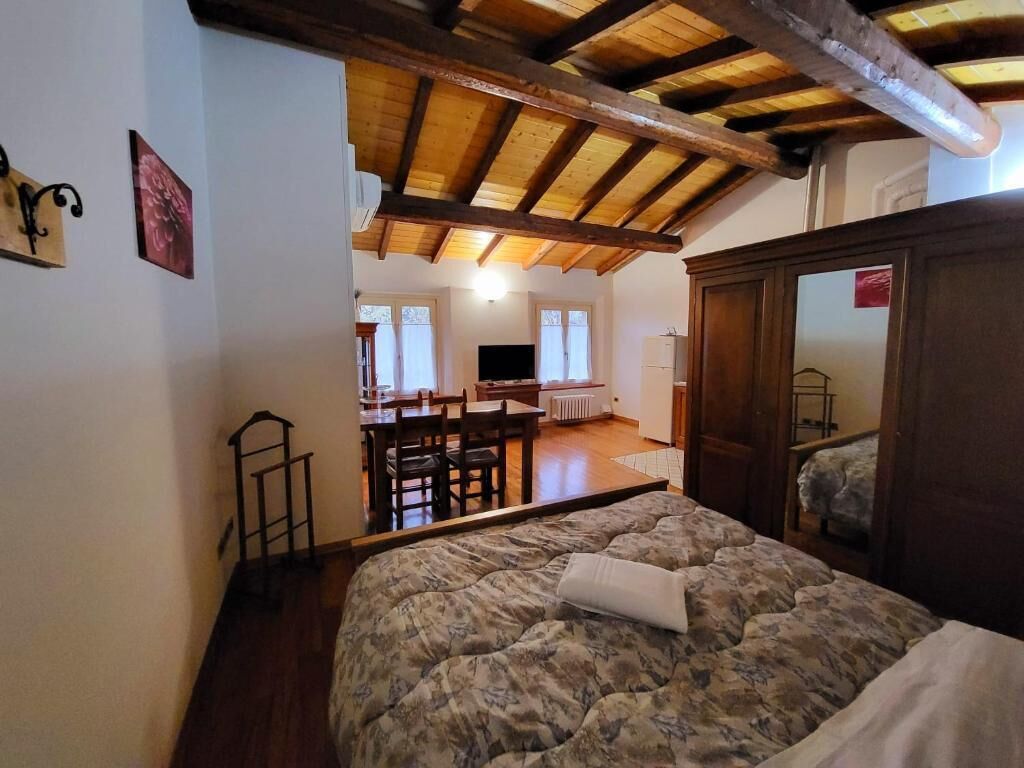 Ein Schlafzimmer mit Bett, Holzbalkendecke, Schreibtisch und Stuhl im Hintergrund.