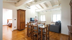 A dining area with a wooden table and chairs, a cabinet, and a television in the background. - Residence Antico Borgo (Modena)