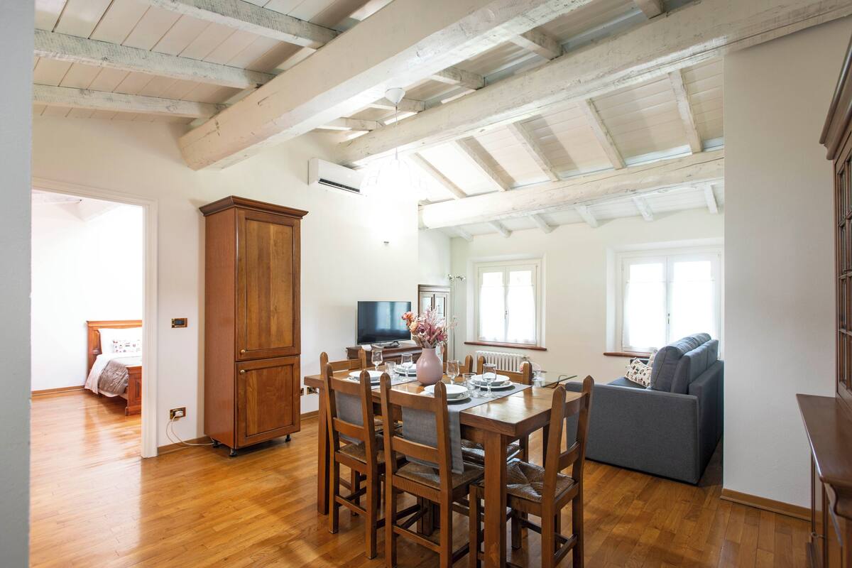 A dining area with a wooden table and chairs, a cabinet, and a television in the background.